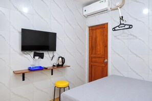 Een kamer met een bed, een aan de muur bevestigde televisie, een houten deur en een kleine tafel met een waterkoker en glazen.