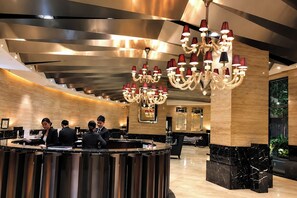 A modern hotel lobby with a reception desk, multiple chandeliers, and a large mirror. - Spacious The Gramercy Residences (Makati)