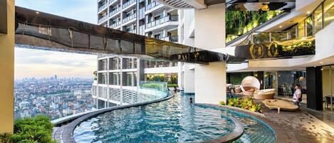 Una piscina interior moderna con diseño curvo, rodeada de abundante vegetación y vistas a un paisaje urbano.