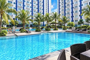 A swimming pool with lounge chairs and palm trees, surrounded by a high-rise building with balconies. - Jazz Residences (Makati)