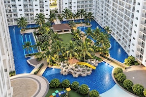 A large indoor swimming pool surrounded by palm trees and a rock formation, with a building in the background. - Shore Residences Moa Pasay (Pasay)