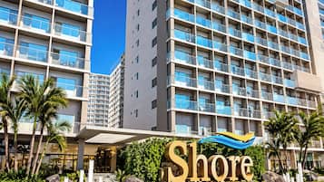 Un hotel de varios pisos con un llamativo letrero 'Shore', que presenta un diseño arquitectónico moderno con balcones y un cielo despejado.