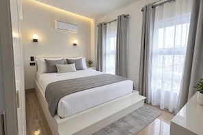A modern bedroom with a bed, bedside tables, a wall-mounted air conditioner, and a view through sheer curtains. - Victoria Sports Tower - Tomas Morato (Quezon)
