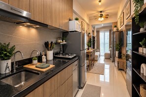 A modern kitchen with stainless steel appliances, wooden cabinets, and a black countertop. - Coast Residences Moa (Pasay)