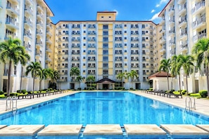A hotel with a central swimming pool, multiple balconies, and palm trees. - Smdc Fields Field Residences Sucat (Parañaque)