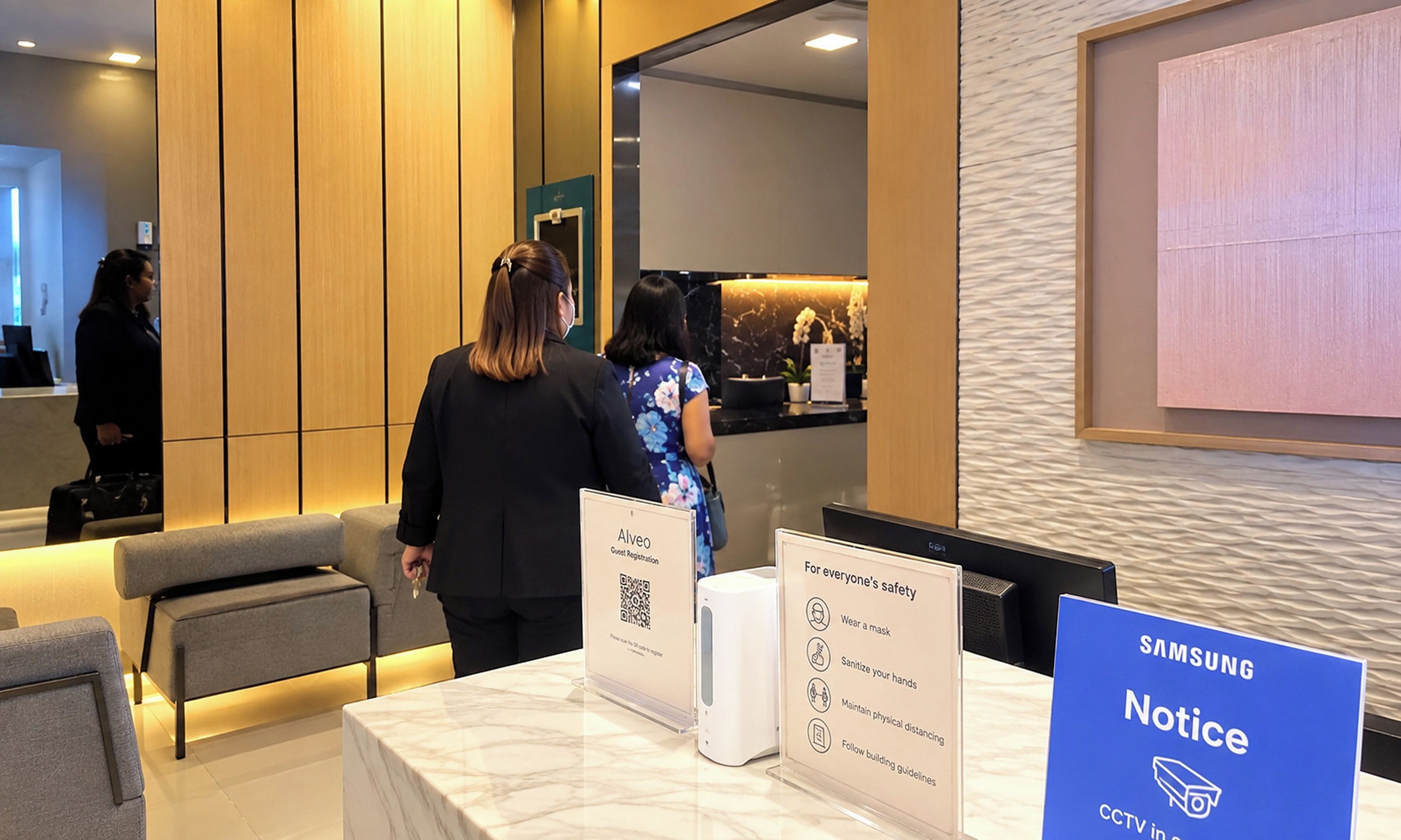 A hotel reception area with a Samsung notice sign, a guest registration kiosk, and a seating area.
