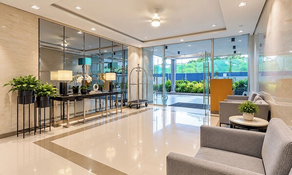 Un vestíbulo moderno con mostrador de recepción, zona de estar y puertas de cristal que dan a un jardín exterior.