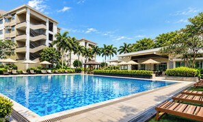 Una piscina con sillones de descanso y sombrillas, rodeada de edificios altos y palmeras.