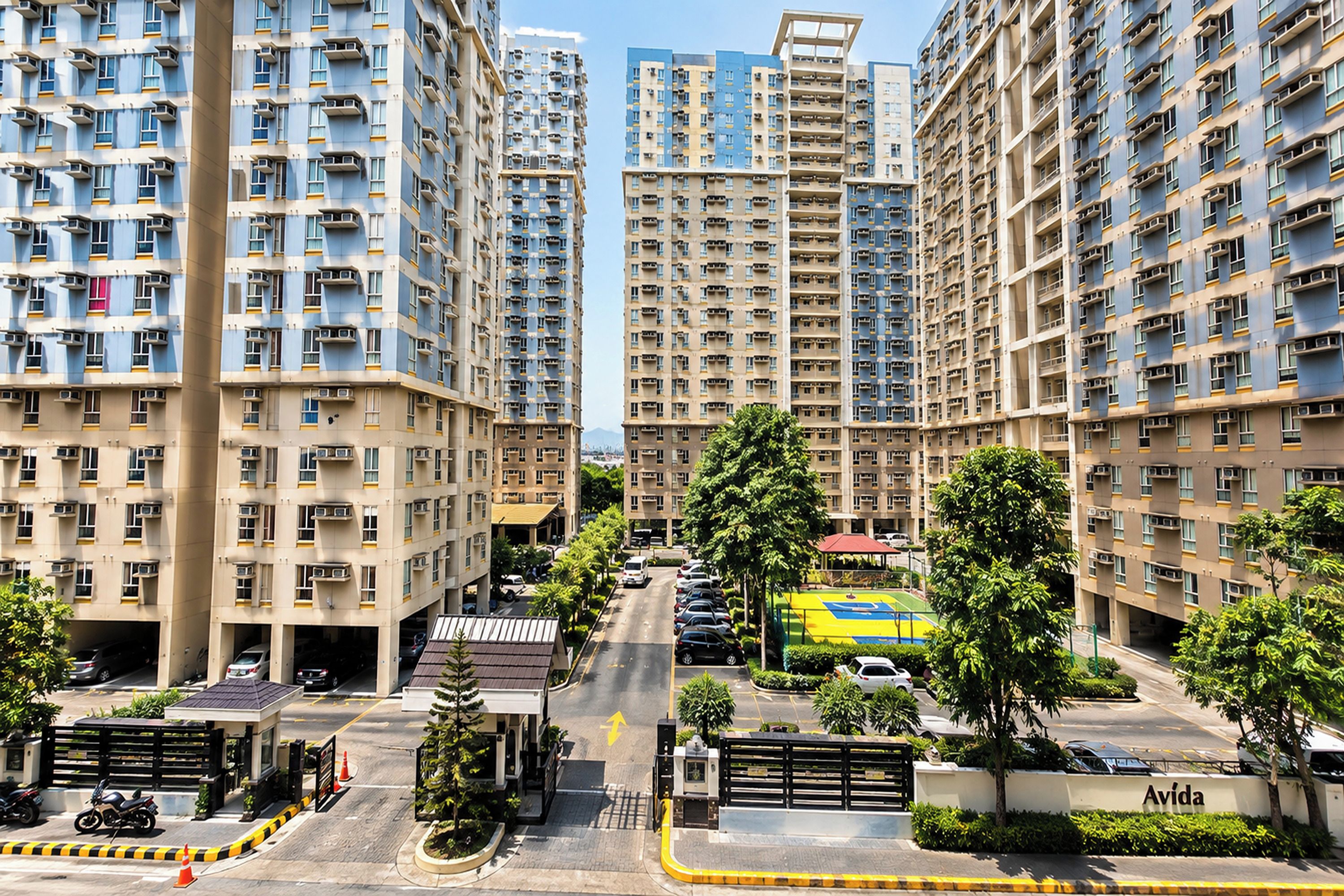 A high-rise residential building with multiple balconies, a gated entrance, and a clear sky.