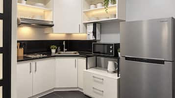 A modern kitchen with white cabinets, a stainless steel refrigerator, a microwave, and a kettle.