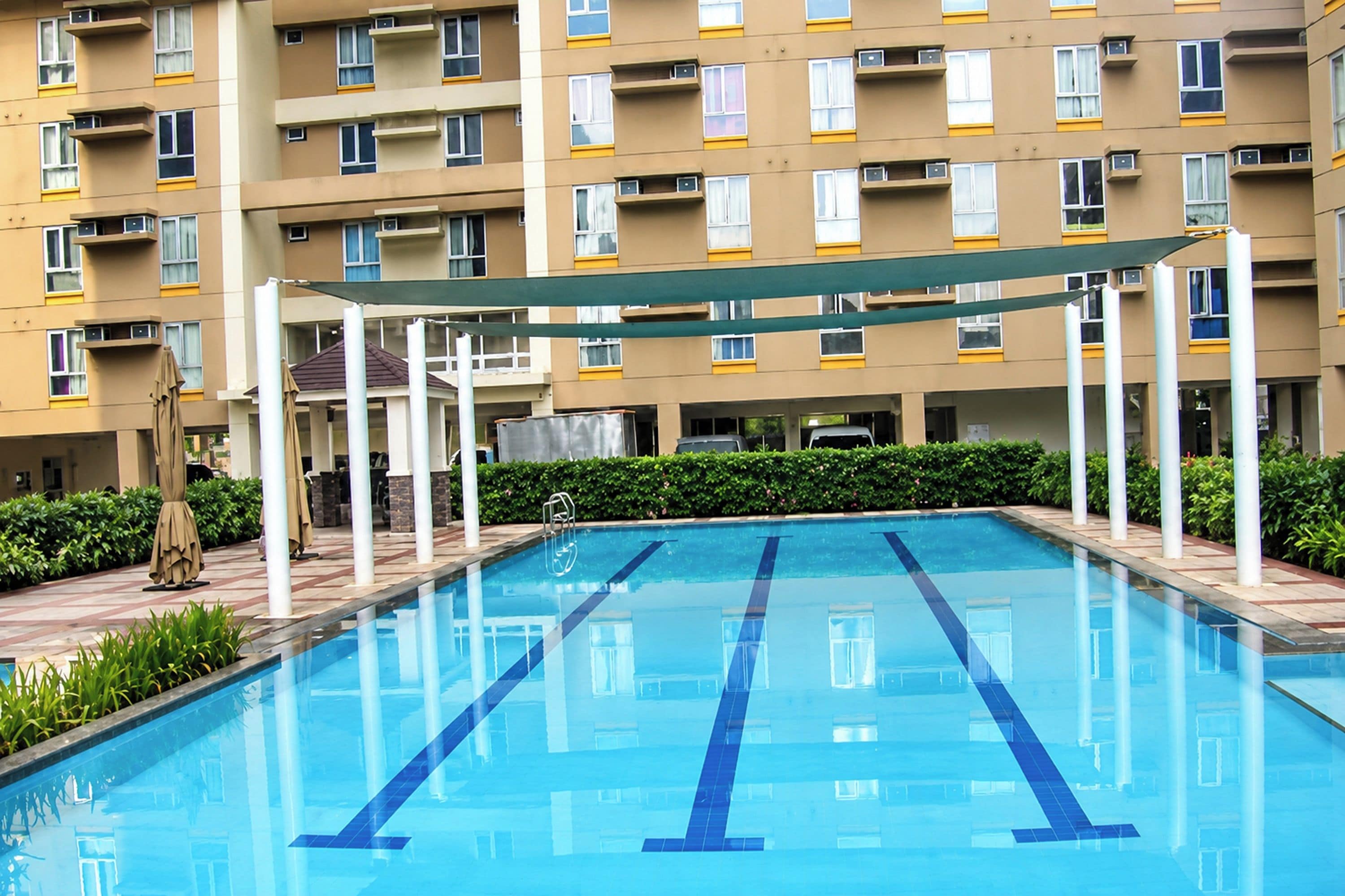 A swimming pool with a clear blue water surface, surrounded by a building with multiple balconies and windows.