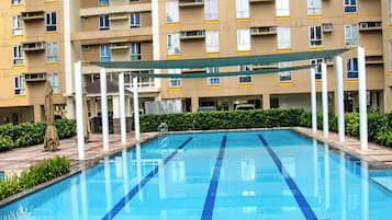 A swimming pool with a clear blue water surface, surrounded by a building with multiple balconies and windows.