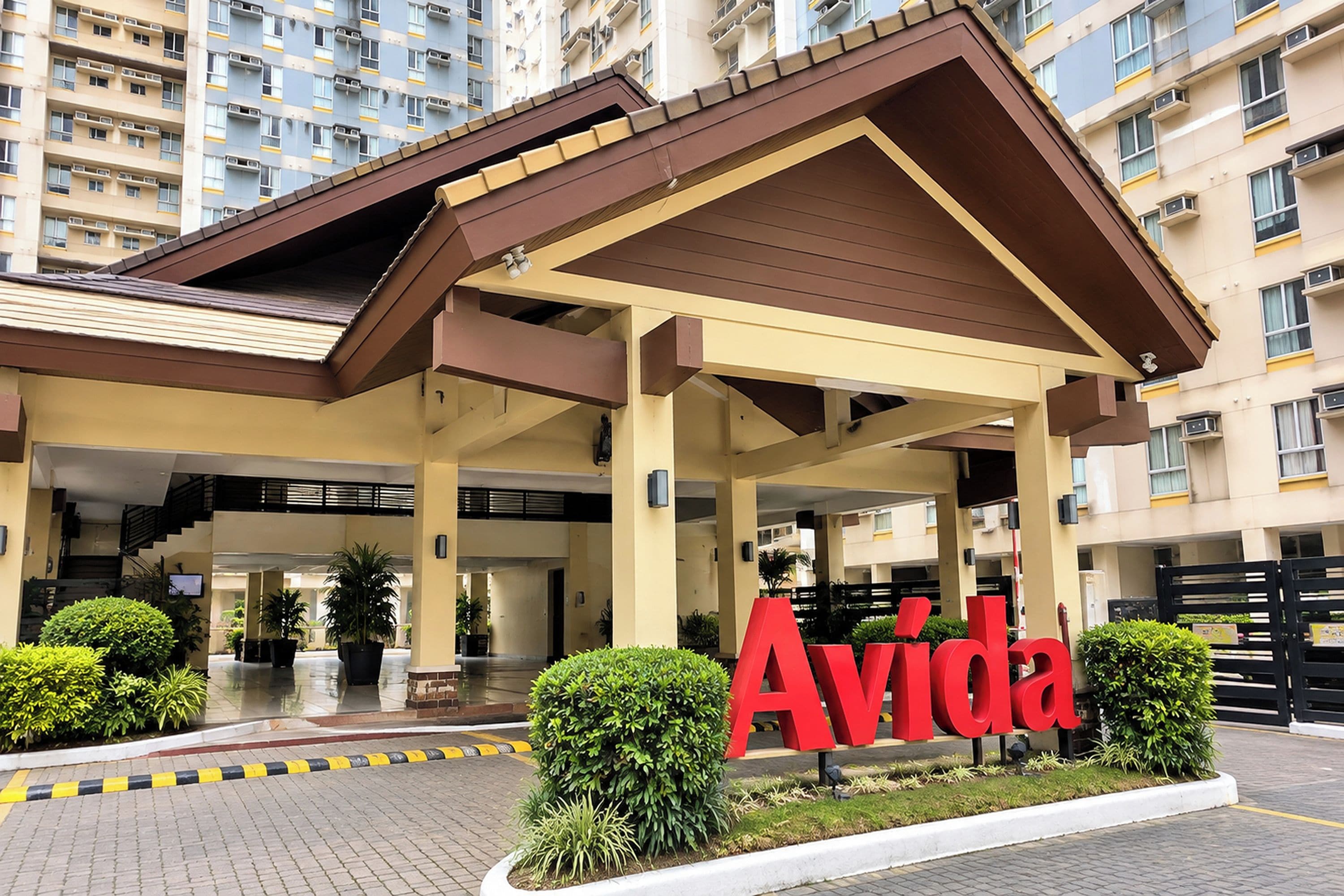 A hotel entrance with a prominent 'Avida' sign, a covered waiting area, and a parking lot.