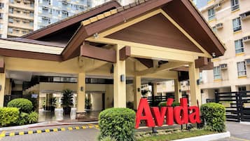 A hotel entrance with a prominent 'Avida' sign, a covered waiting area, and a parking lot.