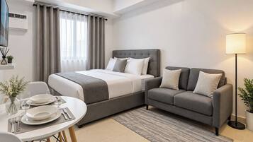 A hotel room with a bed, a sofa, a dining table set for two, and a lamp.