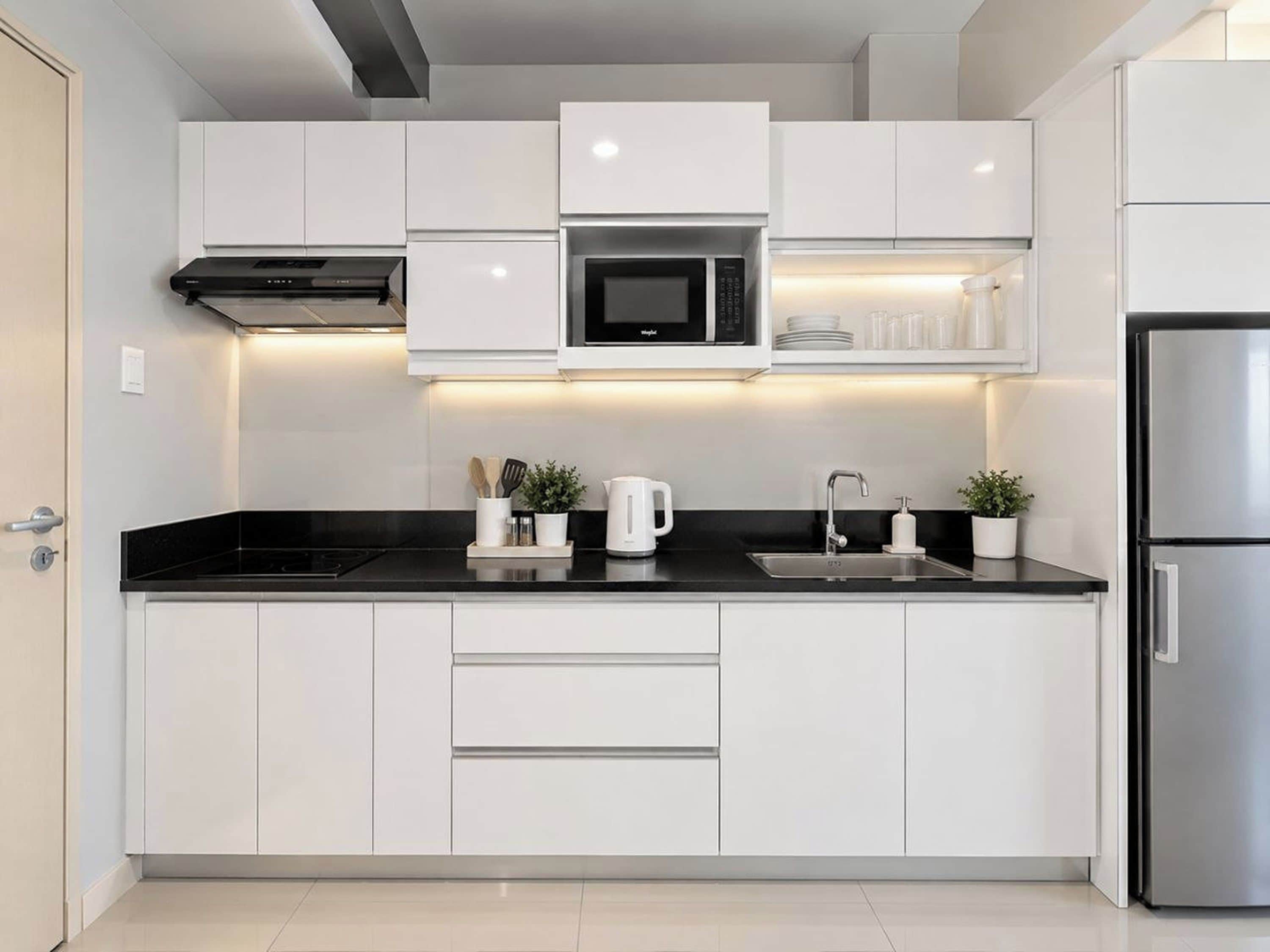 A modern kitchen with white cabinets, a stainless steel refrigerator, a microwave, and a black countertop.