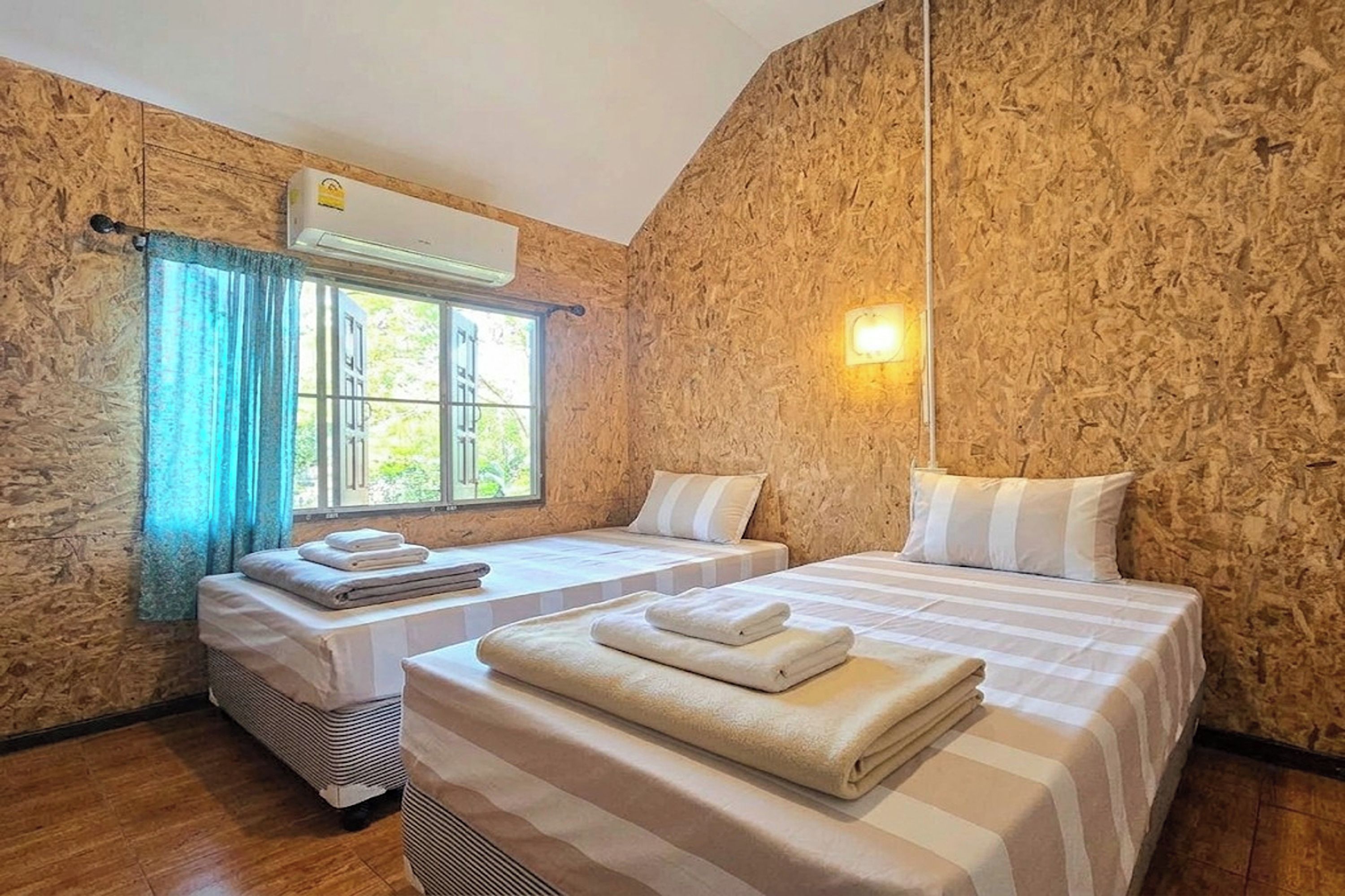Ein Zimmer mit zwei Betten, einem fenster mit Vorhängen, einer Klimaanlage und einer wandmontierten Leuchte.