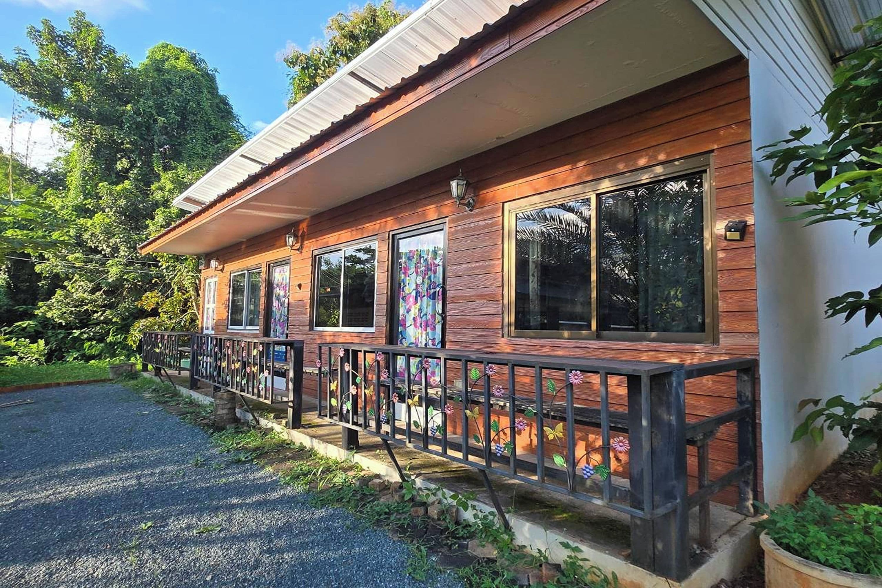 Ein Holzhaus mit Veranda, großen Fenstern und einer Schotterauffahrt.
