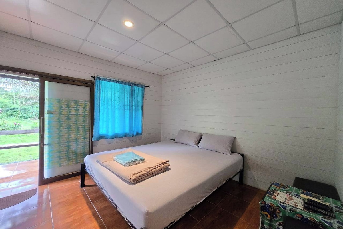 Un dormitorio con cama, ventana con cortinas y vistas al verde exterior.