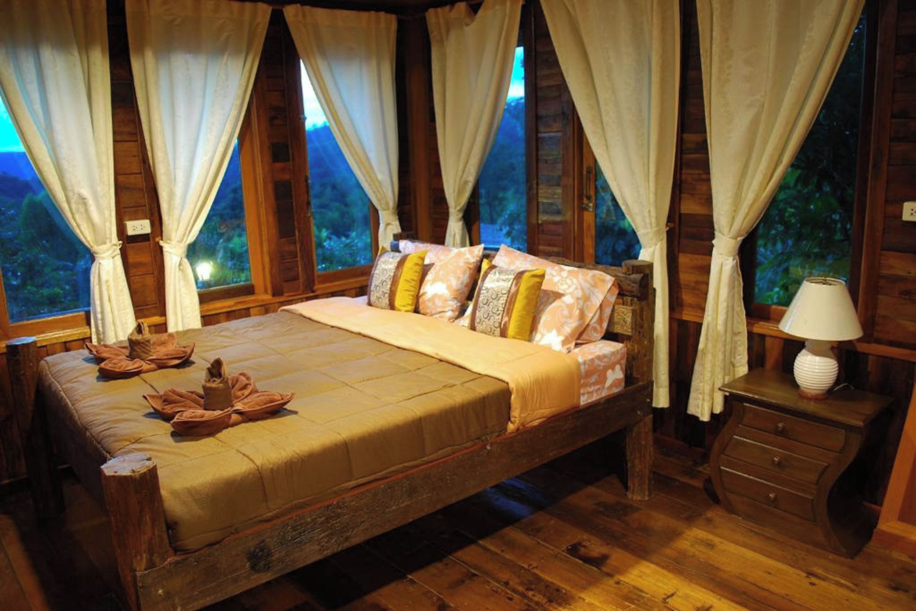 A wooden room with a bed, curtains, and a nightstand.