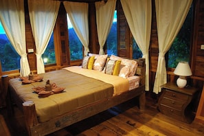 A wooden room with a bed, curtains, and a nightstand.