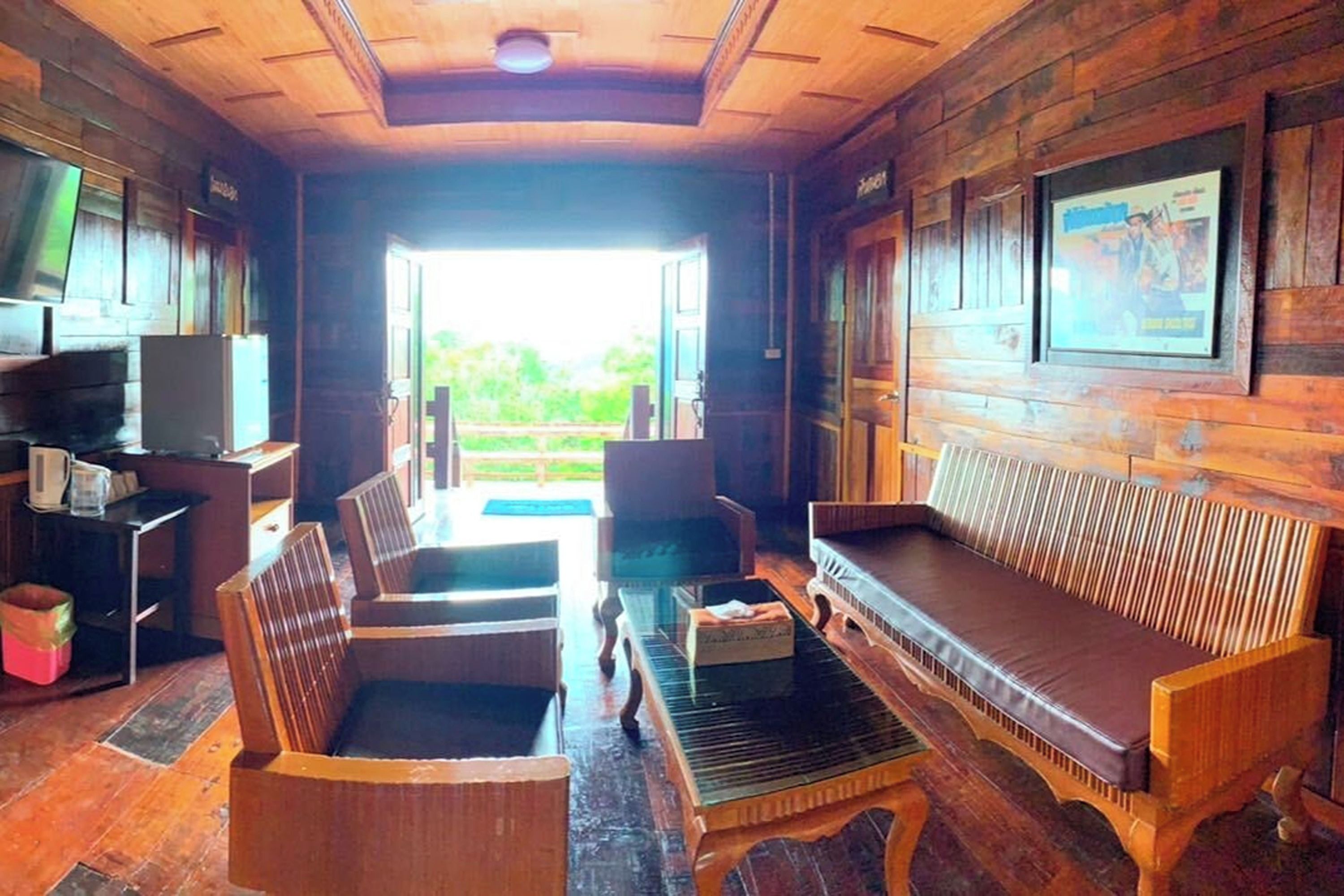 A wooden interior with a sofa, chairs, a television, and a view of greenery outside.