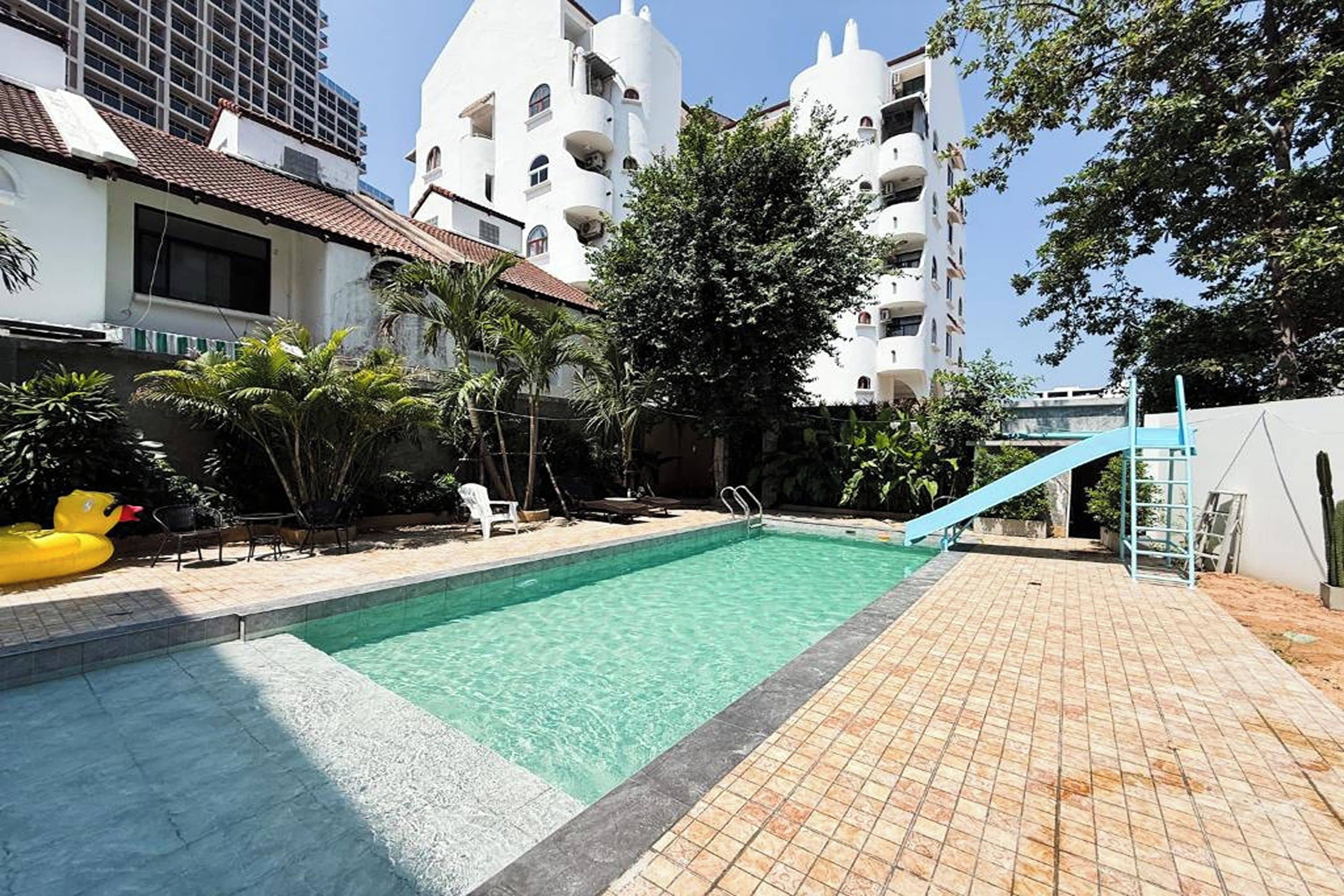 A swimming pool with a slide, surrounded by a tiled deck and palm trees.