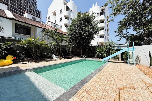 A swimming pool with a slide, surrounded by a tiled deck and palm trees. - Cocoon Hideaway (Pattaya)