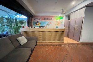 A reception area with a wooden counter, a couch, and a mural depicting a beach scene. - Cocoon Hideaway (Pattaya)