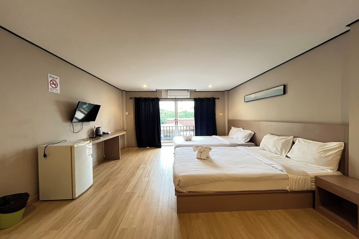 A hotel room with two beds, a desk, a television, and a view of the outdoors.