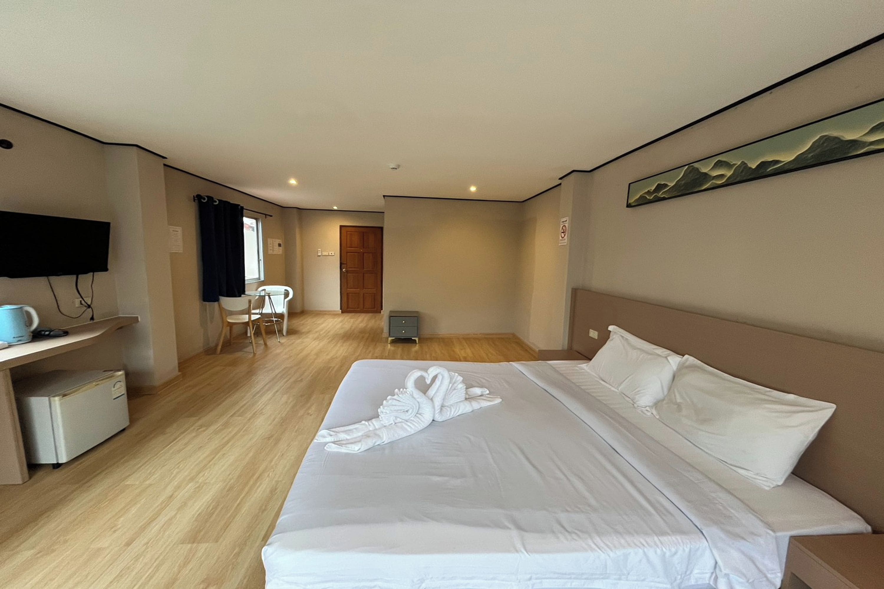 A hotel room with a bed, a desk, a chair, a TV, and a painting on the wall.