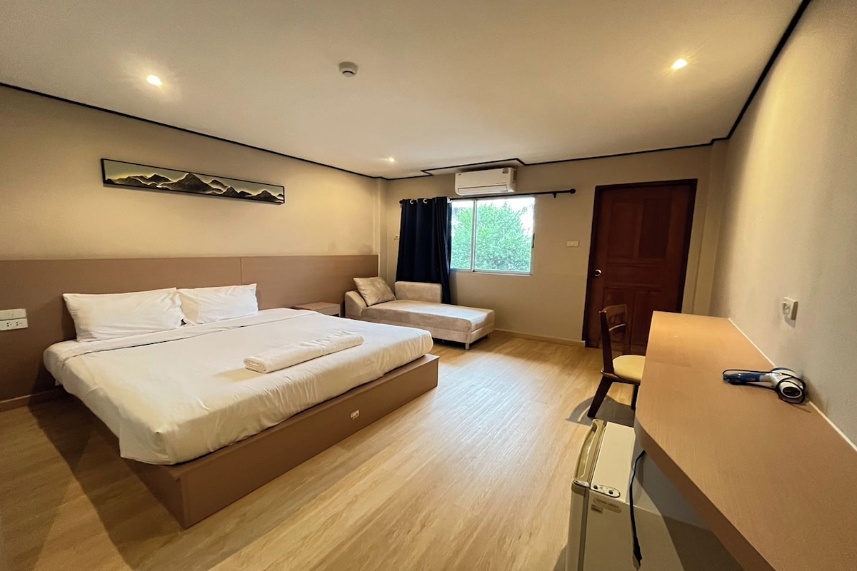 A hotel room with a bed, a seating area, a desk, and a window.