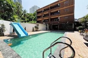 A swimming pool with a slide, surrounded by a brick wall and palm trees. - Cocoon Hideaway (Pattaya)