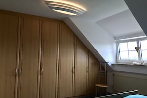 A bedroom with a sloped ceiling, a window with a view, and a wooden wardrobe. - Holiday home with 1 bedroom (Norden-Norddeich)