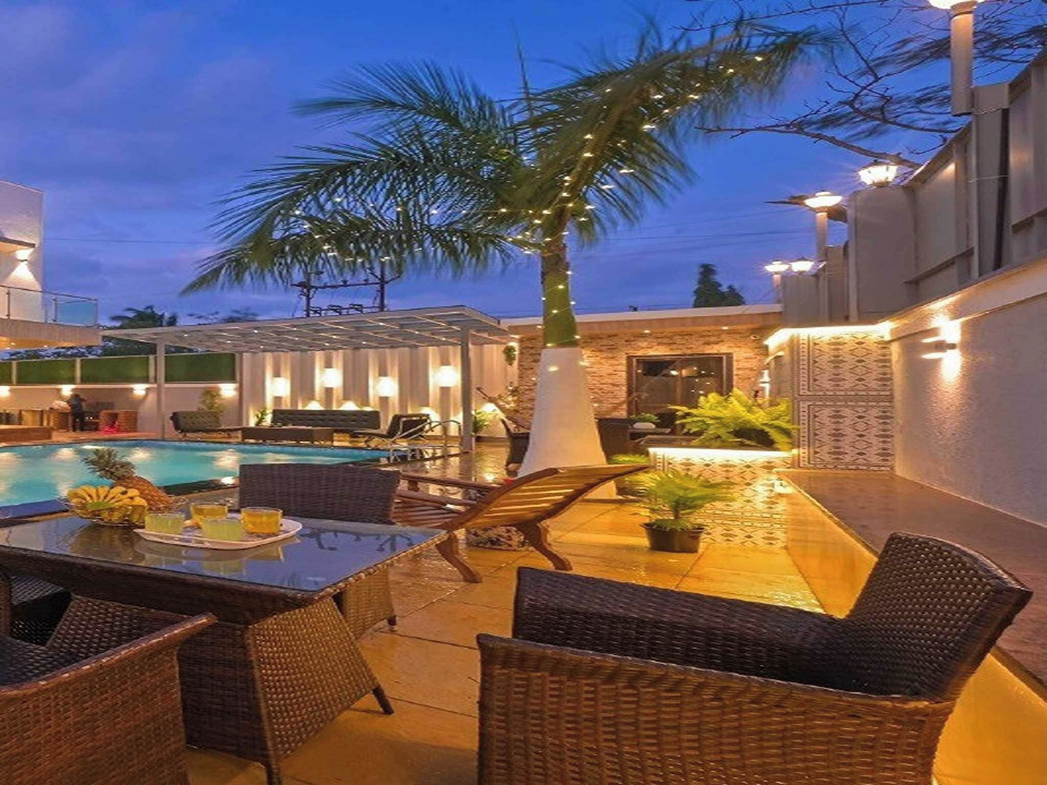 Zona junto a la piscina con mobiliario de mimbre, una mesa de comedor y una palmera.