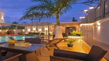 Zona junto a la piscina con mobiliario de mimbre, una mesa de comedor y una palmera.