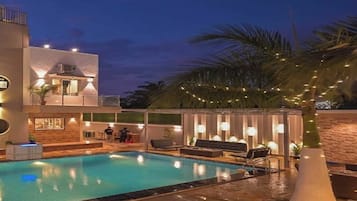 A swimming pool area with a modern building, outdoor seating, and string lights.