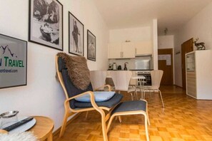 Ein modernes Wohnzimmer mit Holzboden, einer Couch mit Felldecke, einem Esstisch mit Stühlen und einer Küche im Hintergrund.
