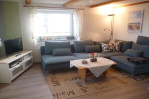 A living room with a sofa set, a television, a coffee table with flowers, and a lamp. - Holiday apartment with 2 bedrooms (Poppenbüll)