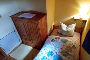 A small bedroom with a wooden wardrobe, a bed with floral bedding, and a bedside table with a lamp. - Holiday apartment with 2 bedrooms (Poppenbüll)