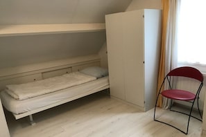 Une petite chambre avec un lit simple, un placard intégré et une chaise.