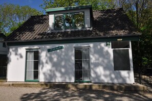 A small, single-story building with a sloped roof, a green-framed window, and a door. - Holiday apartment with 3 bedrooms (Zoutelande)