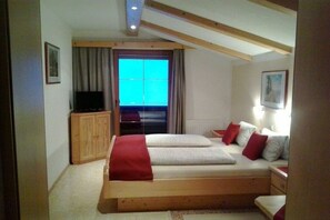 A bedroom with a bed, a television, a wooden cabinet, and a window with curtains. - Holiday apartment with 3 bedrooms (Auffach)