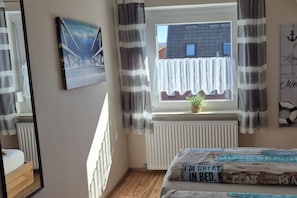 Quarto com cama, janela com cortinas, radiador e quadro na parede.