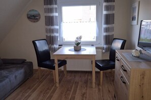 A small dining area with a table, two chairs, a potted plant, and a television on a wooden cabinet. - Holiday apartment with 1 bedroom (Norden-Norddeich)