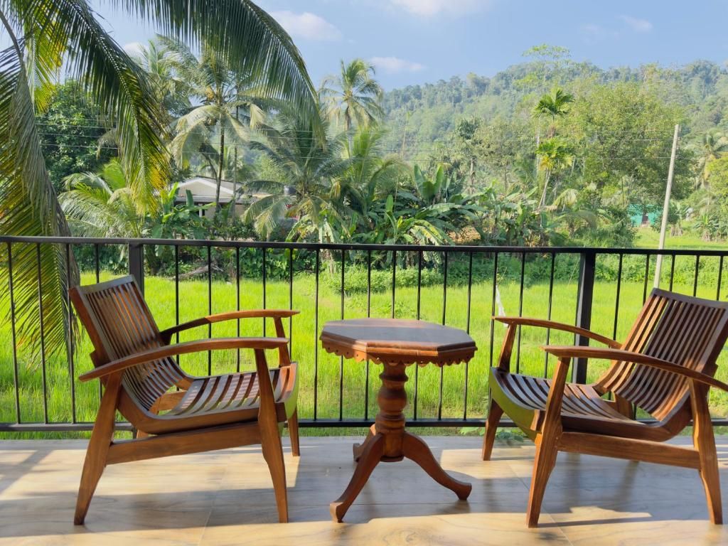 A balcony with two wooden chairs and a small table, overlooking a lush green landscape with palm trees.
