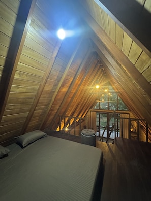 Un dormitorio acogedor en el ático, con techo inclinado, cama, un pequeño rincón de descanso y vistas al exterior.
