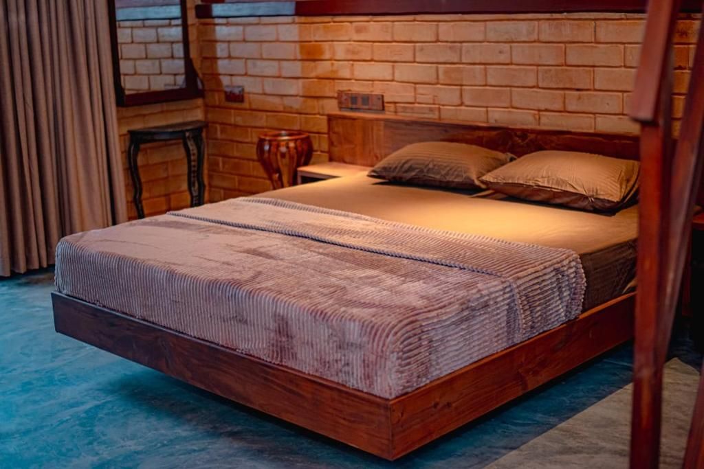 Una cama individual con estructura de madera y una colcha estampada, frente a una pared de ladrillo con ventana y cortinas.