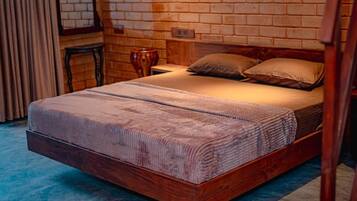 Una cama individual con estructura de madera y una colcha estampada, frente a una pared de ladrillo con ventana y cortinas.