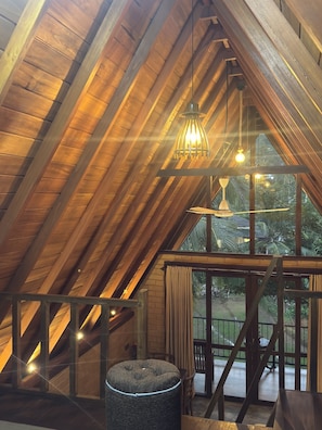 Habitación en ático con vigas de madera, una lámpara colgante, una ventana con cortinas y una escalera.